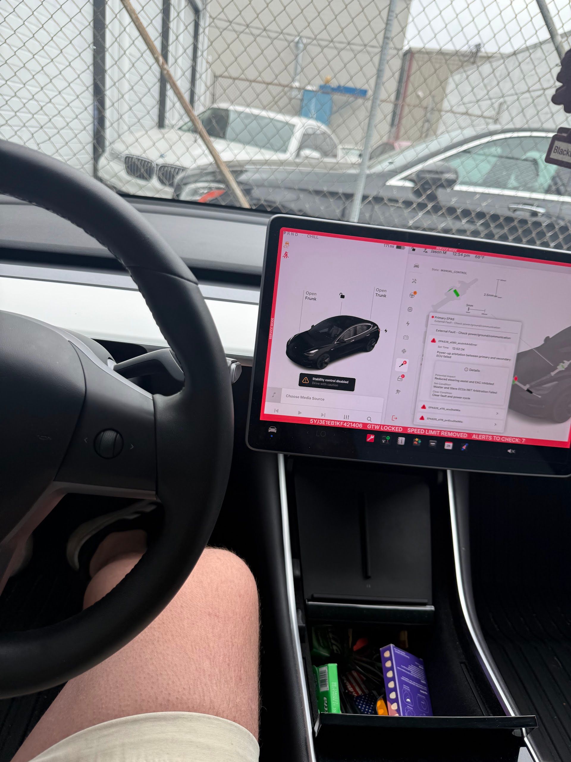 Driver’s seat view with a steering wheel and a tablet showing a car image, parked near a chain-link fence. | Lapin Auto Repair