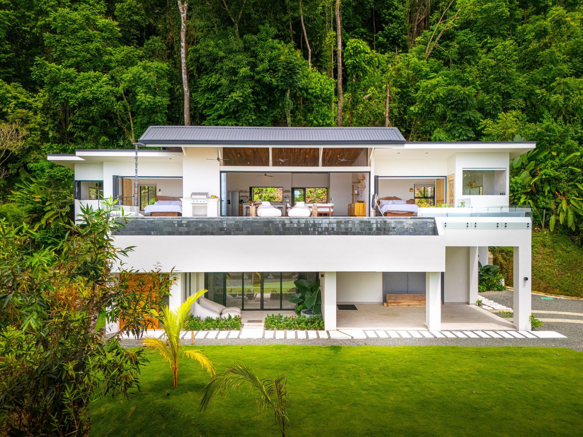 Modern two-story villa with balcony, set in lush green rainforest.
