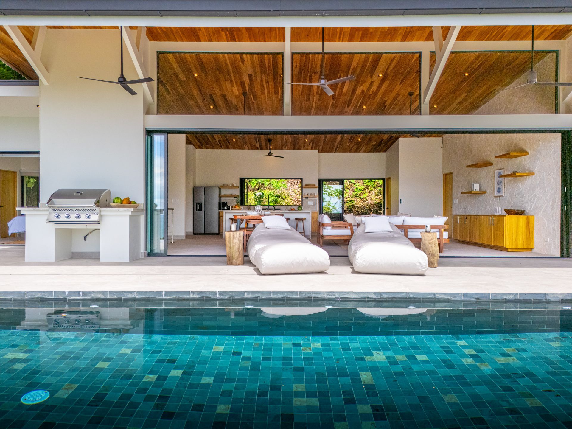 Modern poolside lounge with white seating and a turquoise pool in a bright open-air home