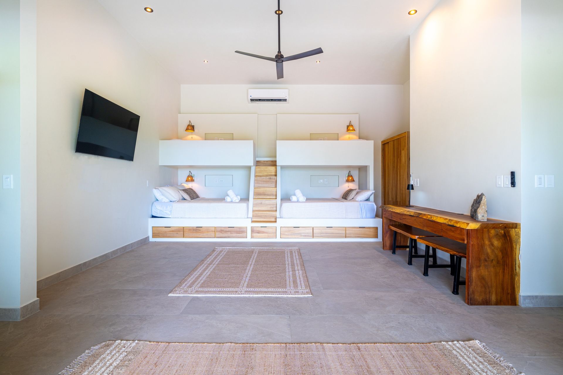 Bright minimalist room with twin beds, wall TV, and wooden desk on the right
