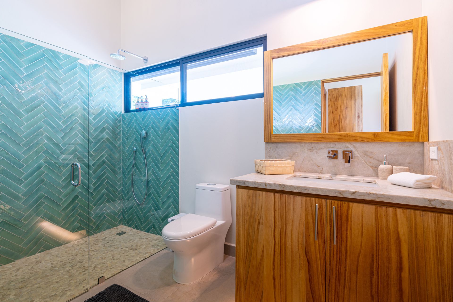 Modern bathroom with glass shower, toilet, and wood vanity with orange-framed mirror