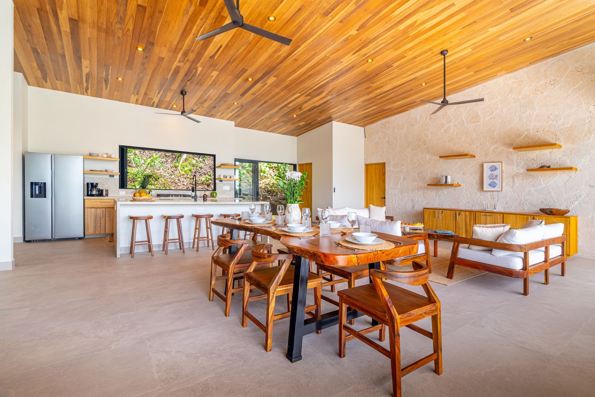 Bright open living area with wooden ceiling, kitchen island stools, and white sofas around a coffee table