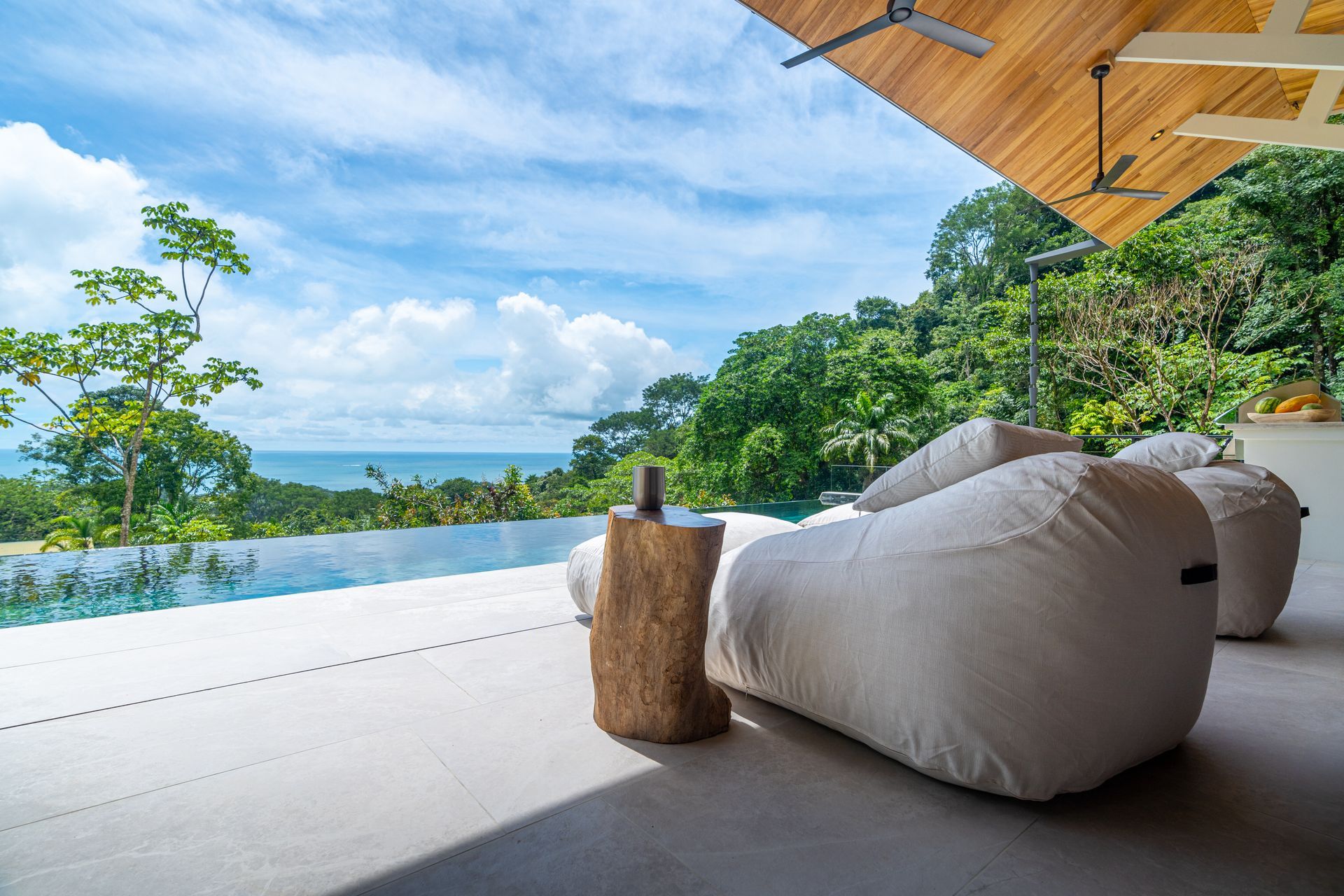 Luxury villa terrace with beanbag seating, infinity pool, and ocean view under a wooden canopy