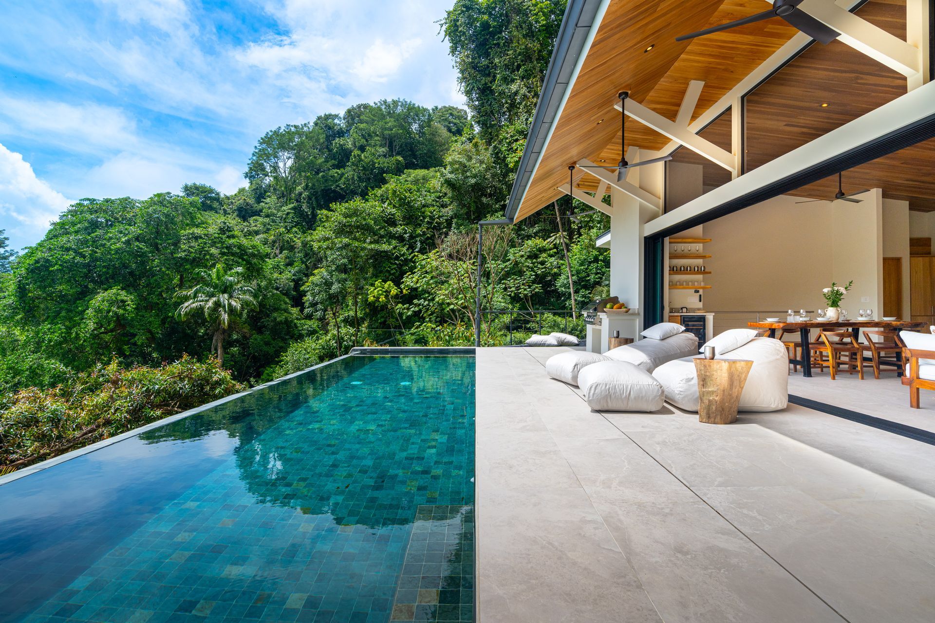 Infinity pool beside modern villa terrace overlooking lush tropical forest