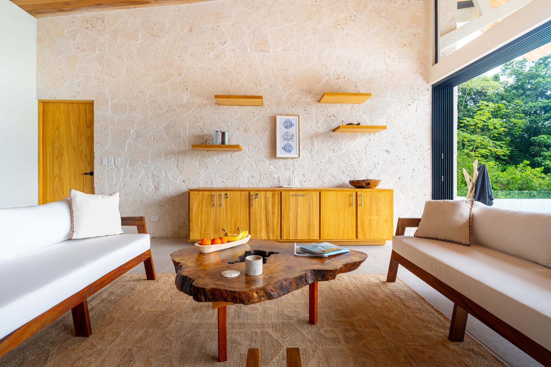 Modern living room with beige sofas, wooden coffee table, sideboard, and large window overlooking greenery