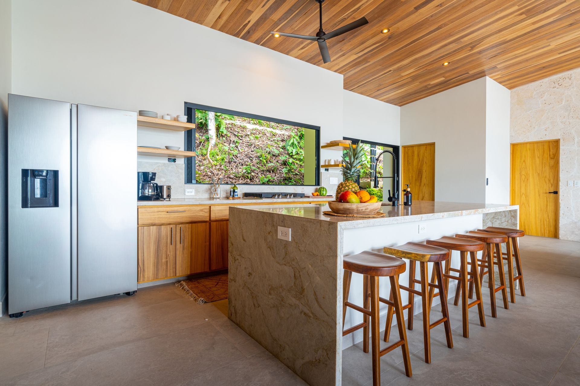 Modern kitchen with wood ceiling, large island, bar stools, and stainless steel refrigerator