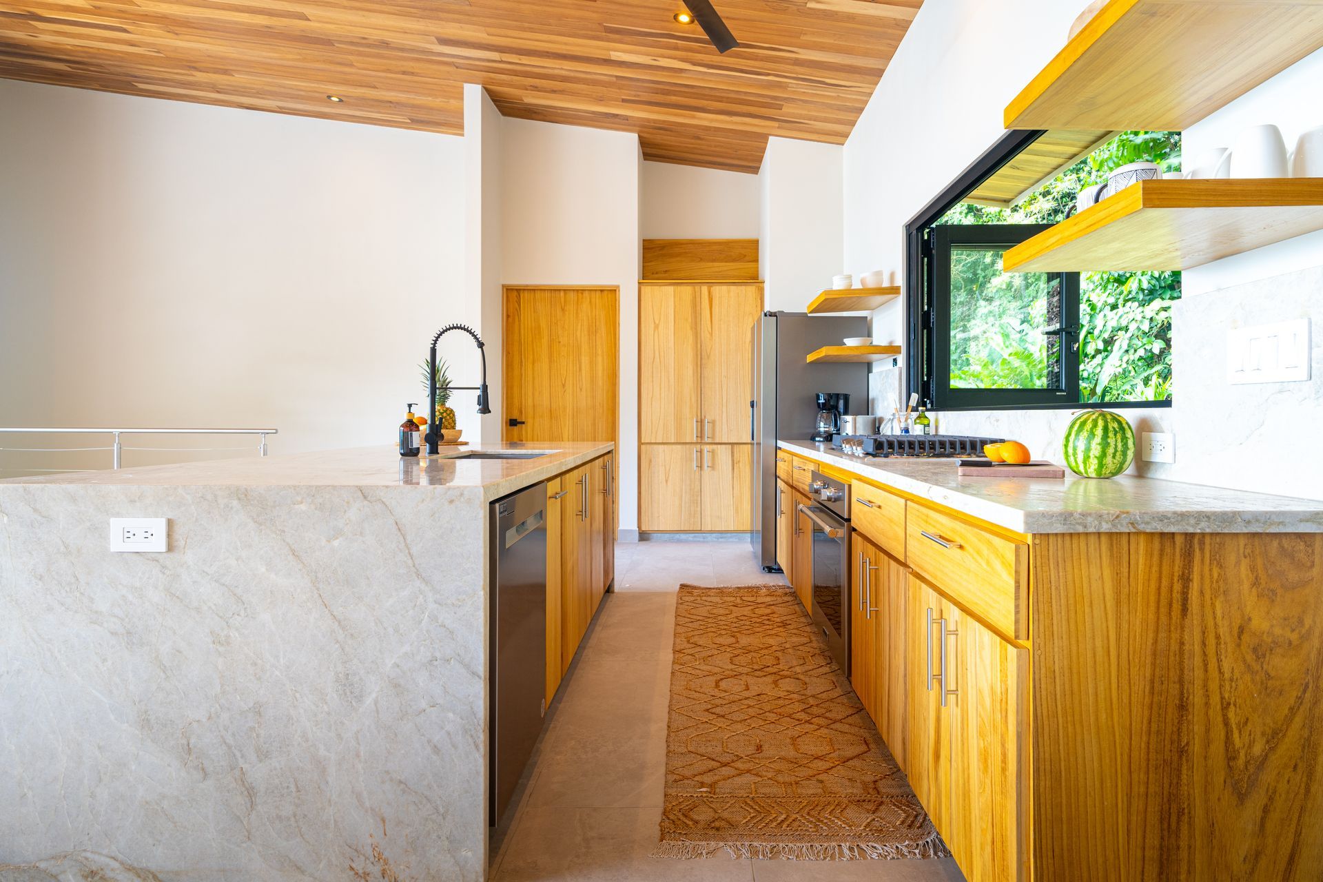 Modern kitchen with wooden cabinets, stone island, skylight, and large window overlooking greenery
