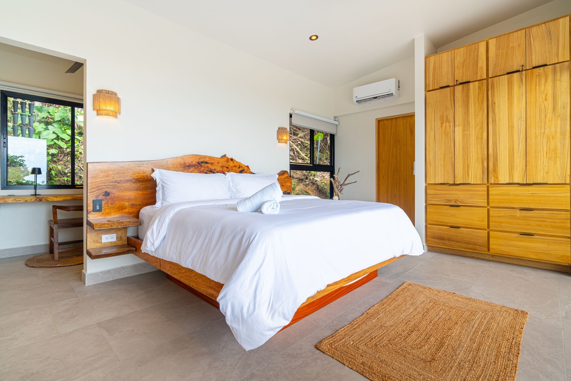 Bright bedroom with a wooden bed, white bedding, wardrobe, and a rug by the window