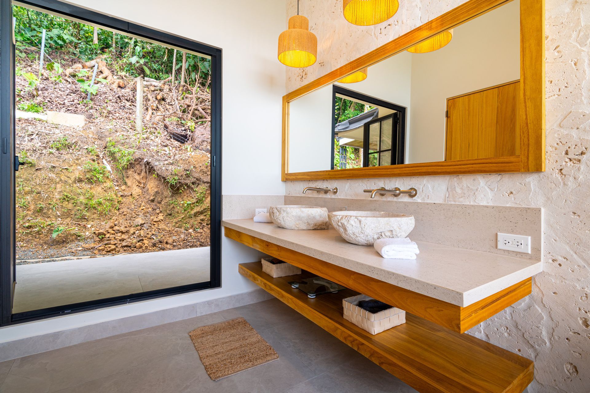 Modern bathroom vanity with wood accents, large mirror, vessel sink, and a window overlooking greenery