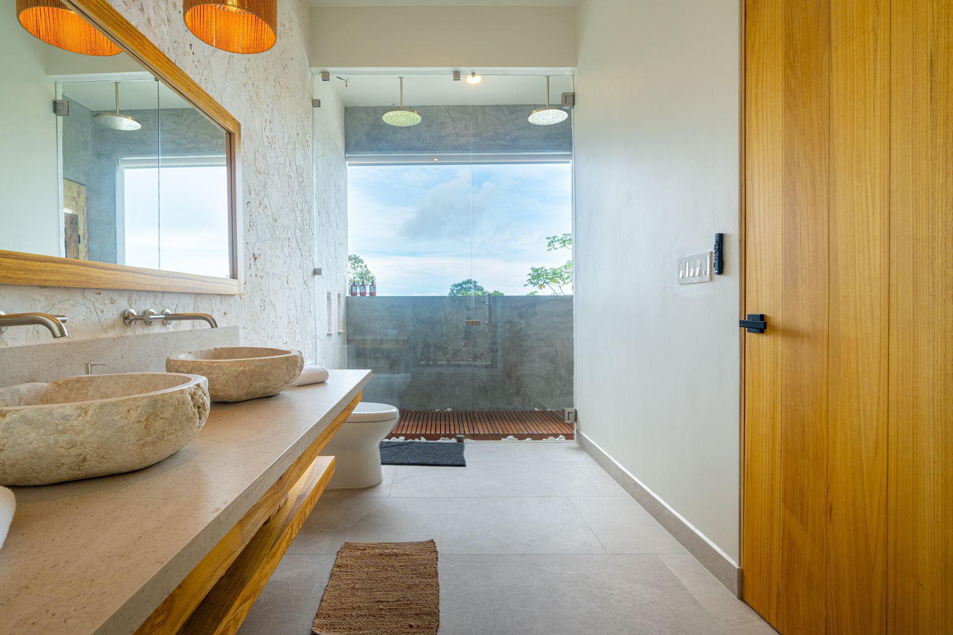 Modern bathroom with double sink vanity, mirror, wooden door, and large window overlooking the ocean
