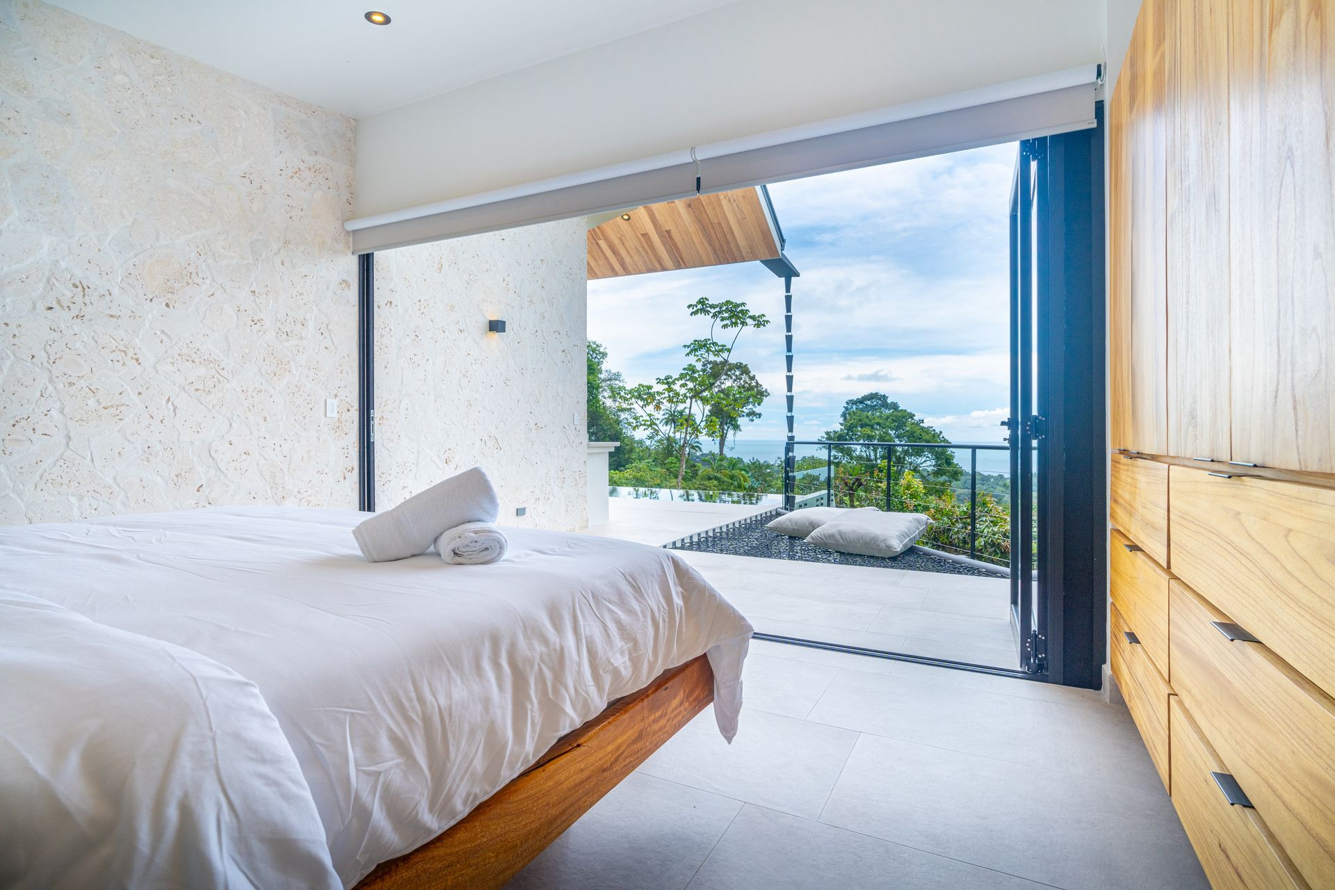 Bright bedroom with bed, open sliding doors, and ocean-view balcony