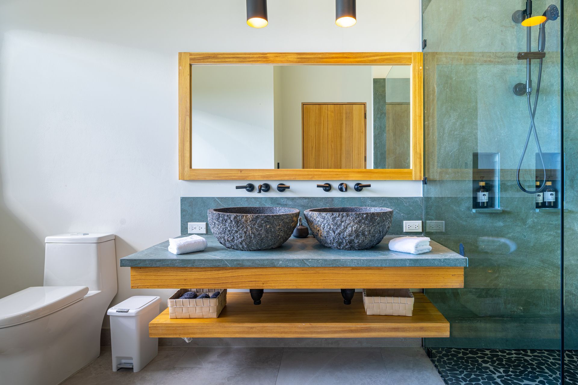 Modern bathroom with floating wood vanity, large mirror, glass shower, and toilet