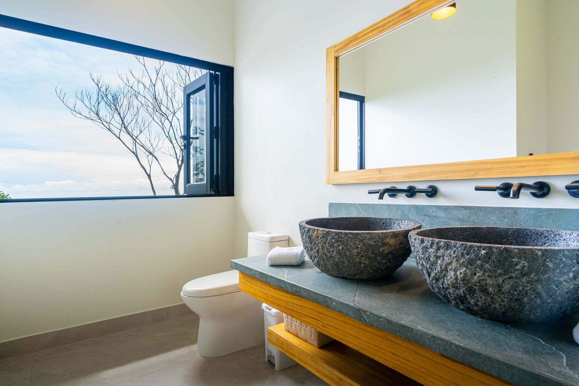 Bathroom vanity with blue window frames, two stone sinks, and a wall mirror overlooking the sea
