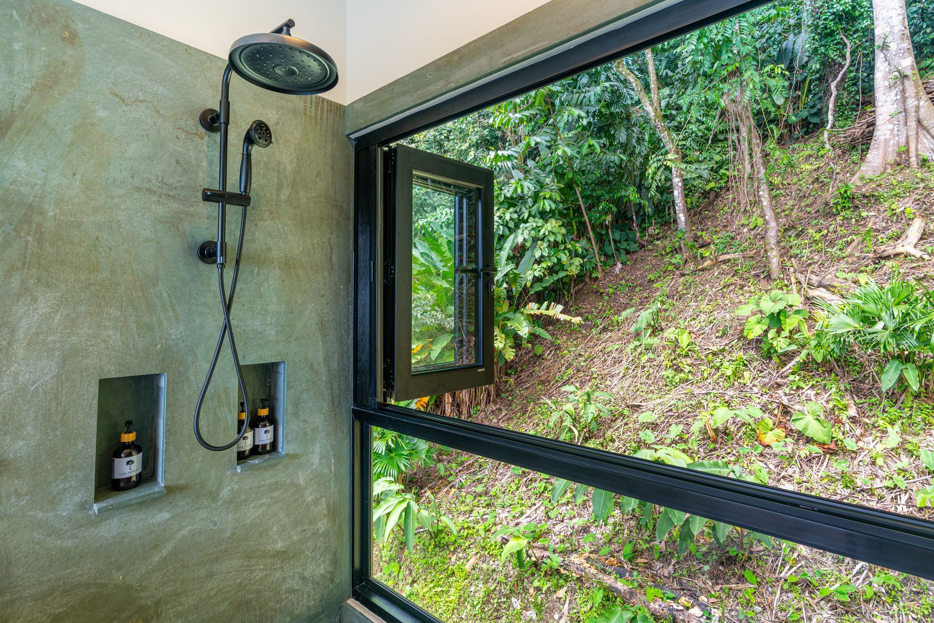 Modern shower with black fixtures beside a large window overlooking a green hillside