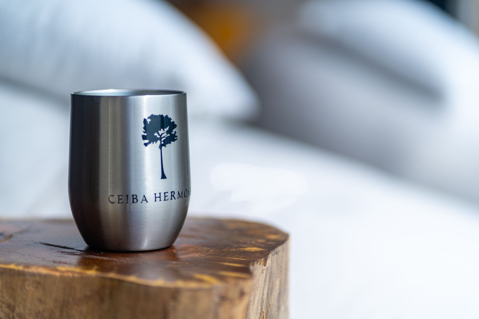 Silver tumbler with tree logo on a wooden surface, against a soft blurred background