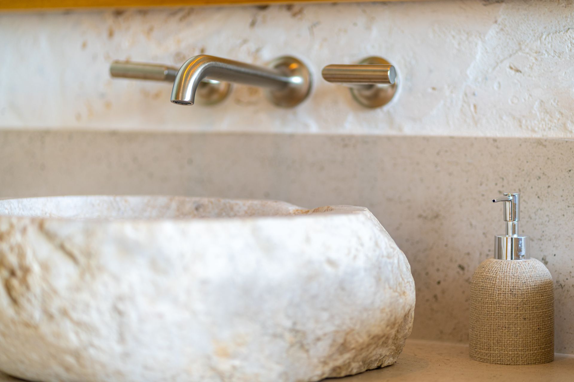 Stone bathroom sink with brass faucet and soap dispenser on a marble countertop
