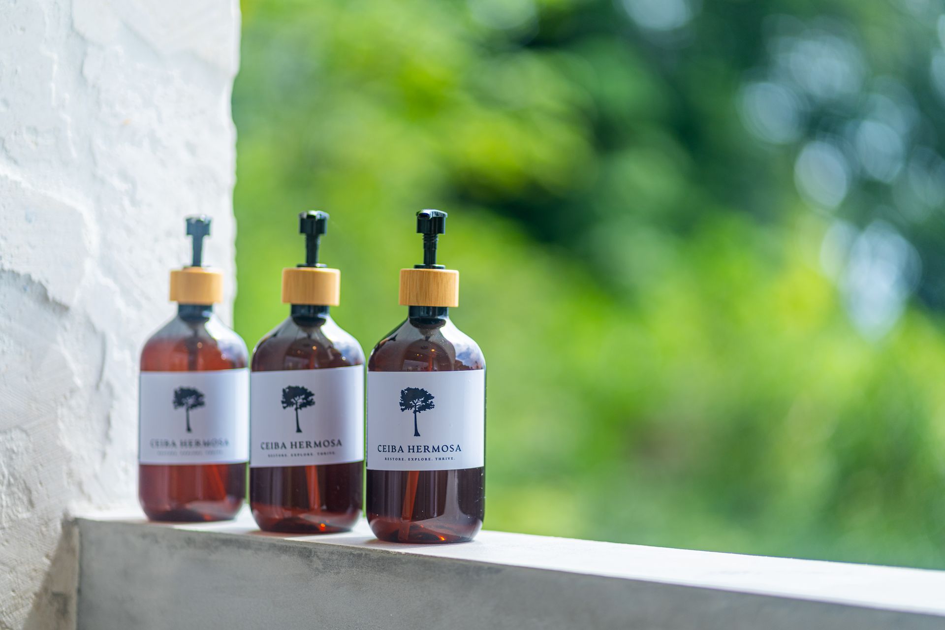 Three amber glass dropper bottles with white labels on a windowsill, against a blurred green outdoor background