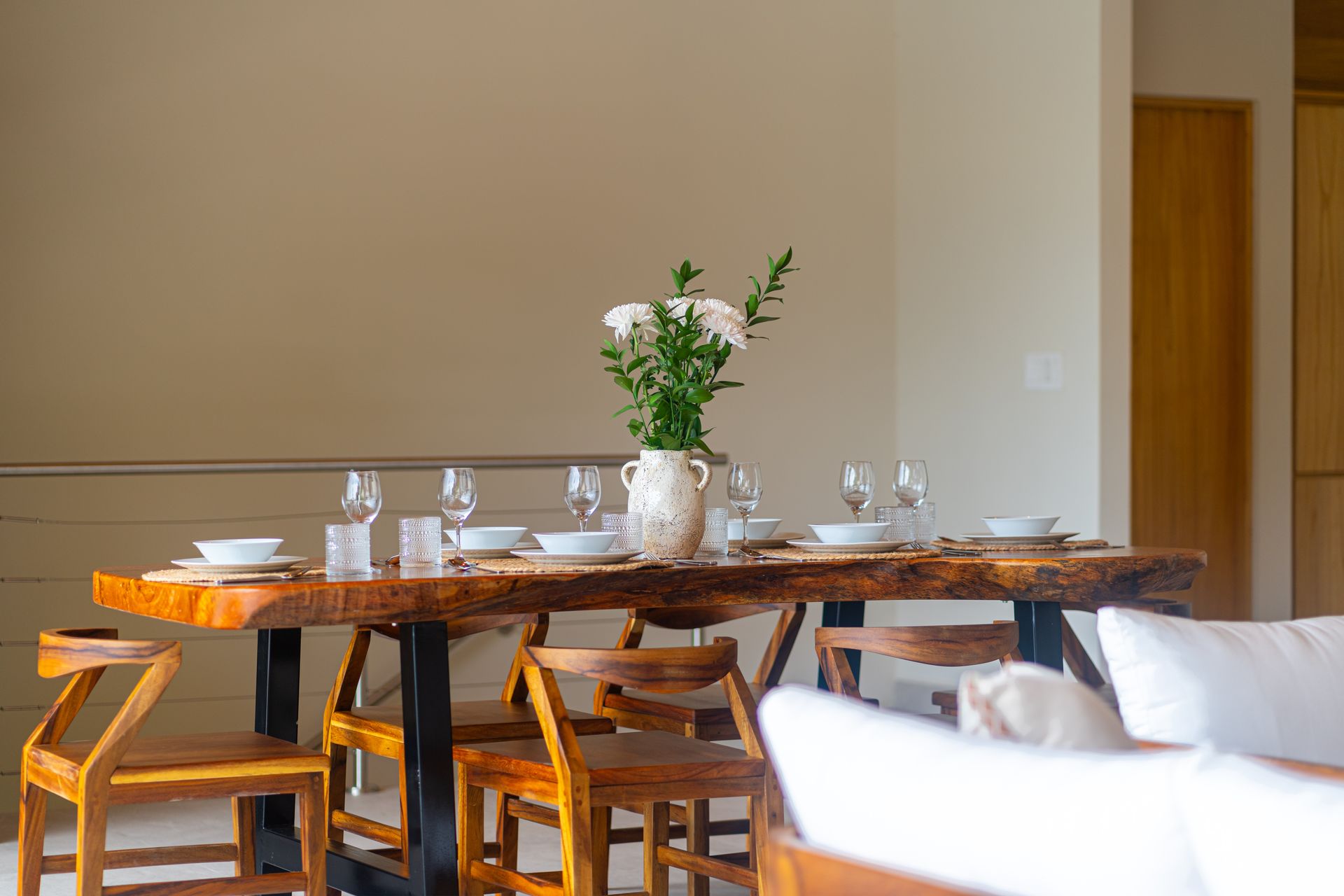 Dining table with glassware, white dishes, and a vase of flowers in a bright room