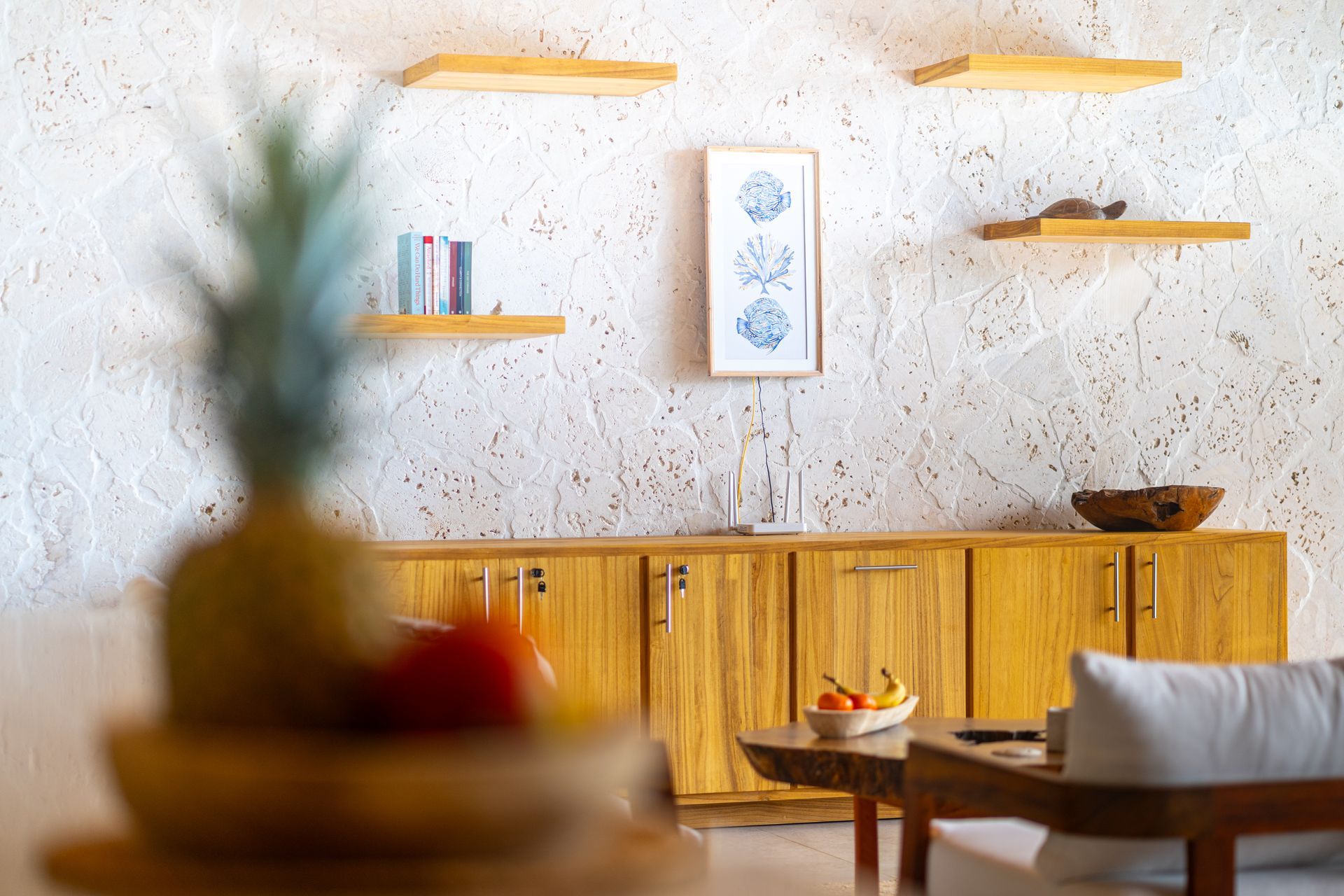 Bright modern living room with wooden cabinet, wall shelves, and a coffee table with fruit centerpiece.