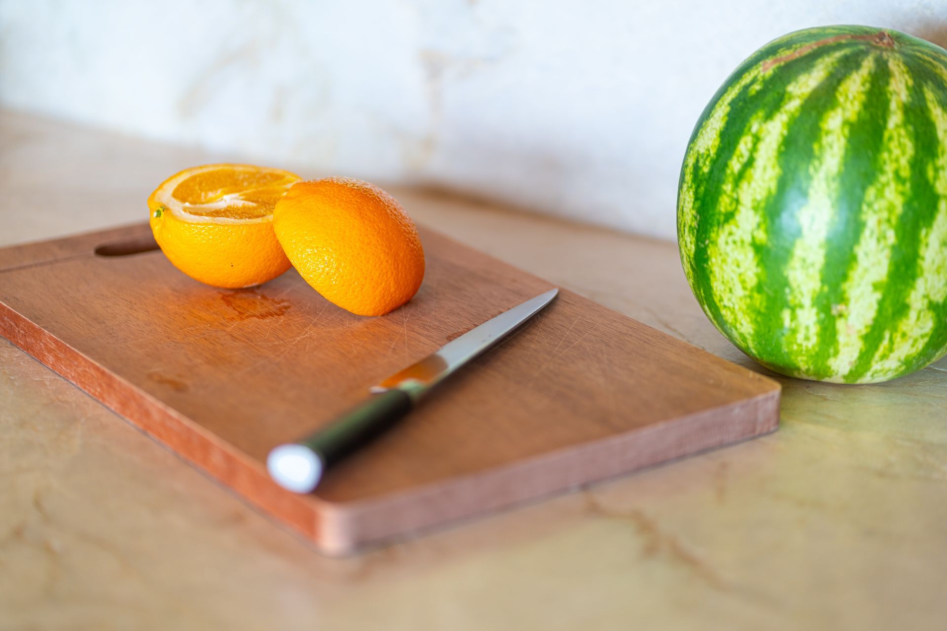Watermelon and sliced orange on a cutting board with a knife on a kitchen counter