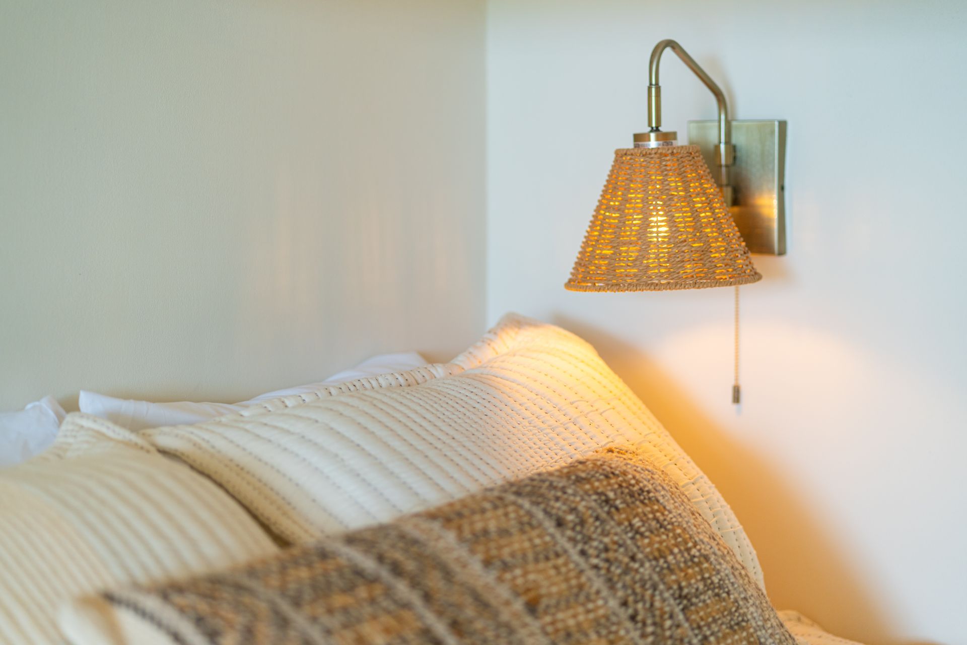 Cozy bed with white pillows and a woven wall lamp casting warm light