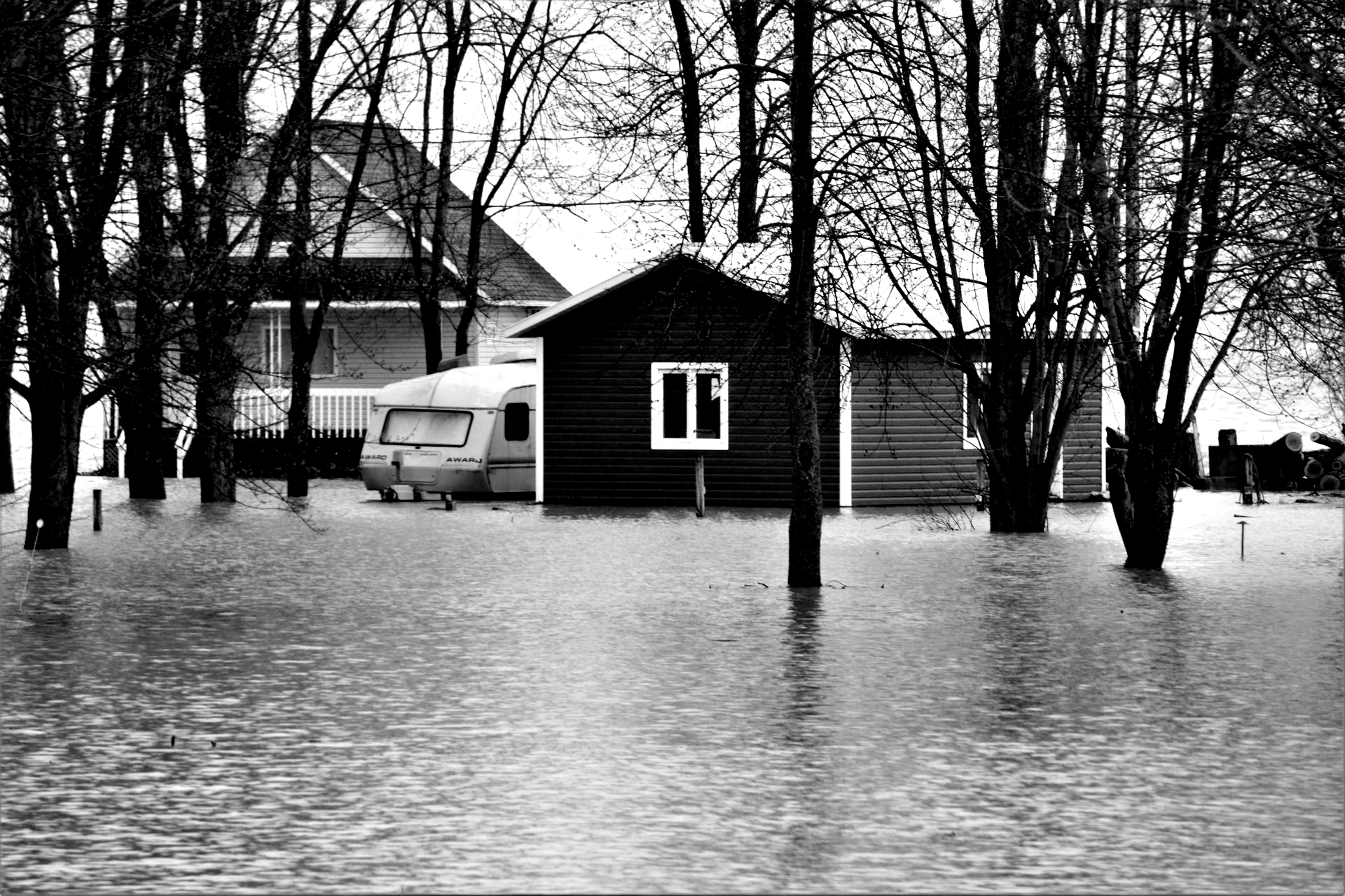 Flooded yard with a small cabin, trees, and a van in standing water; house partially submerged.