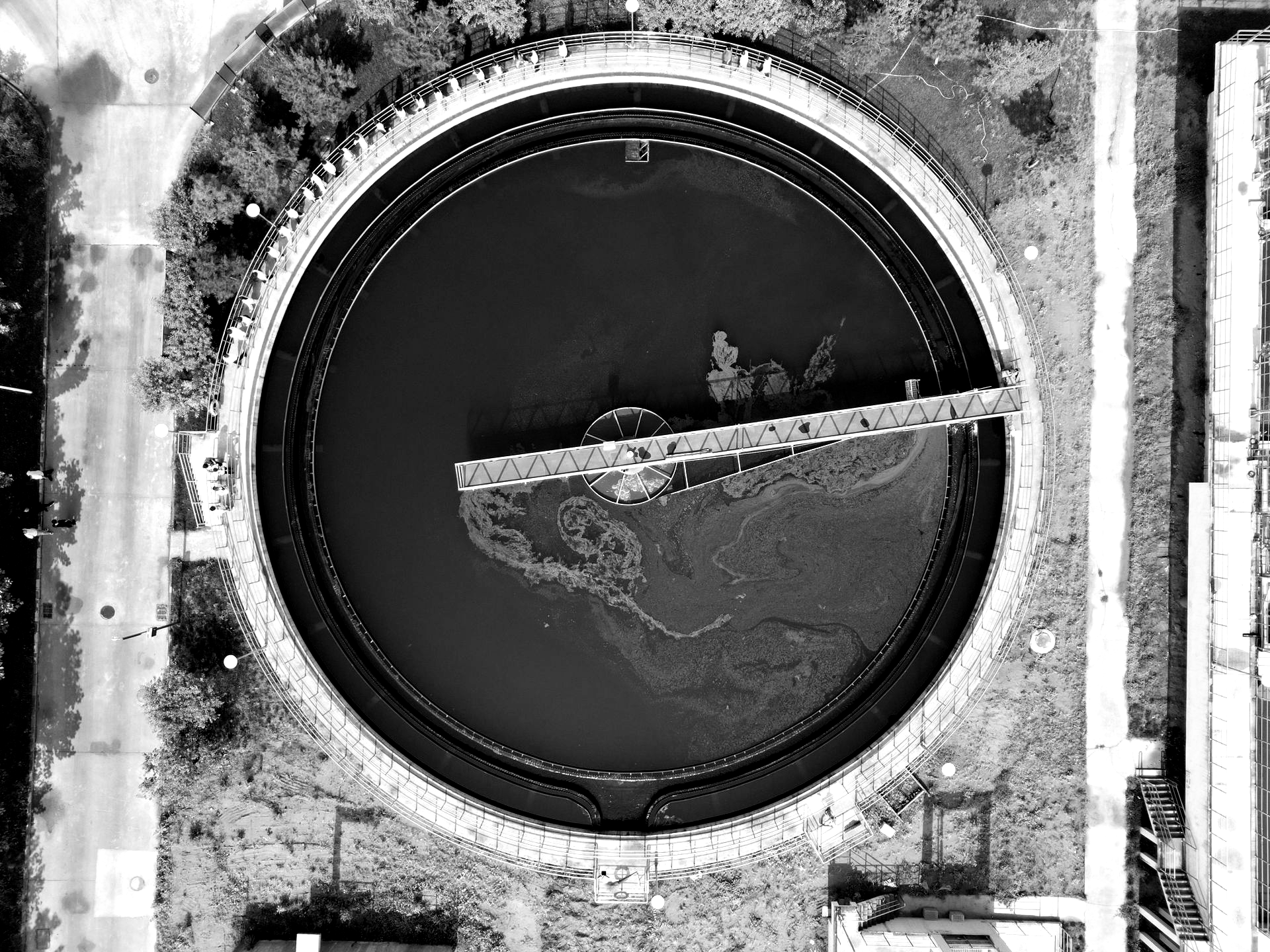 Aerial view of a circular concrete structure with dark water and a diagonal metal barrier inside.