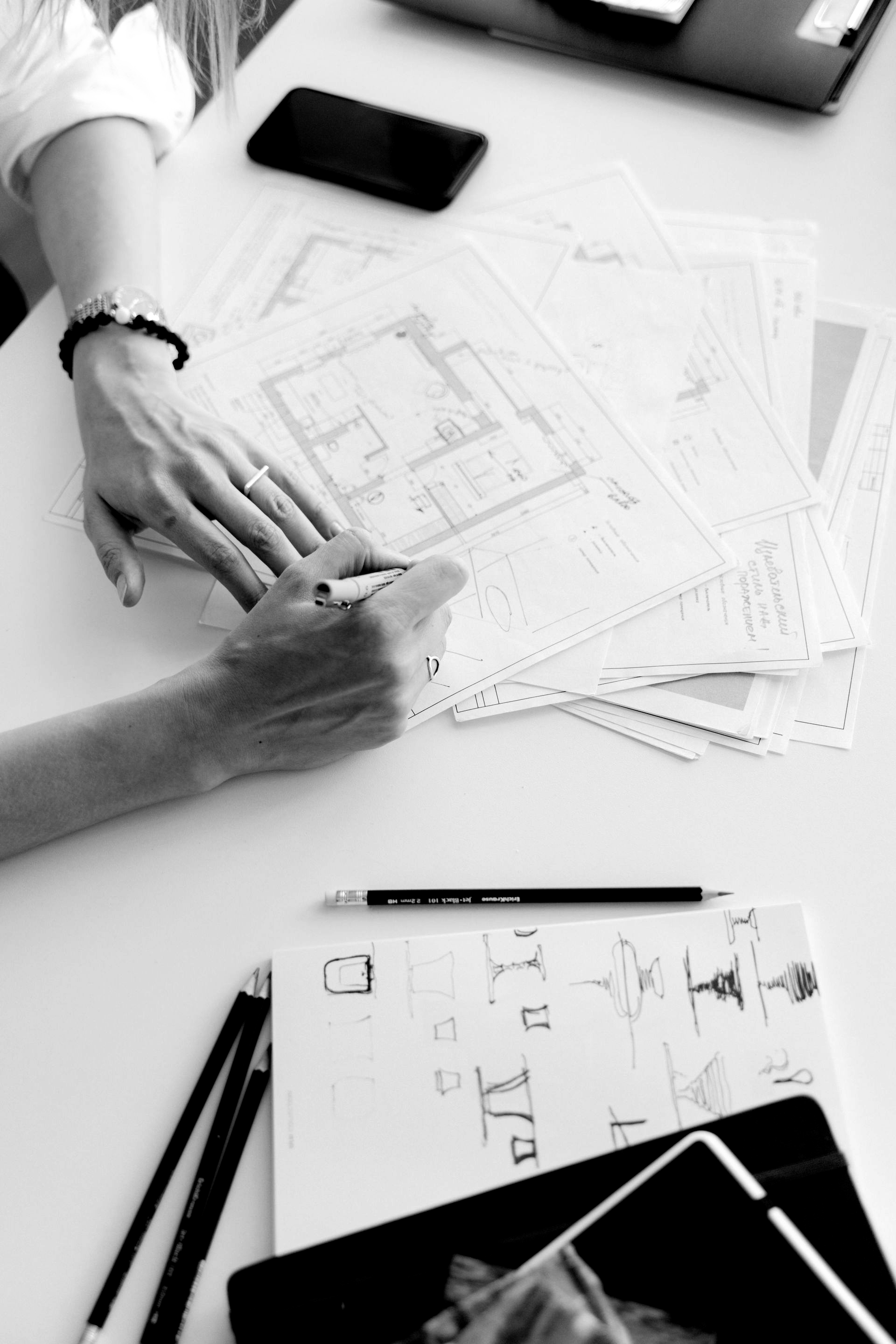 Hands sketching a design layout with pencils and papers on a desk