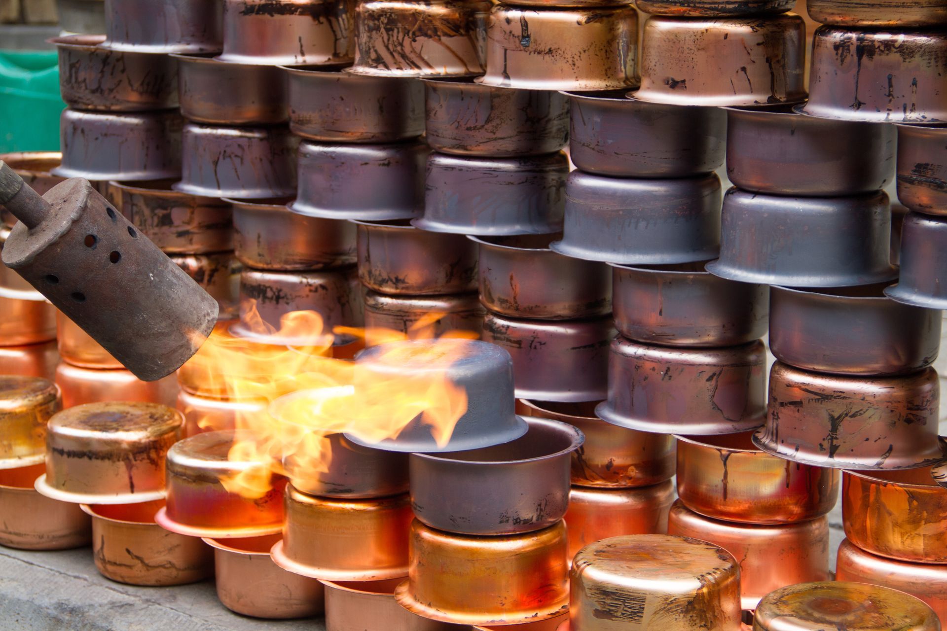 Copper pots being torched with a flame. Some pots are stacked, showing copper and darker tones.