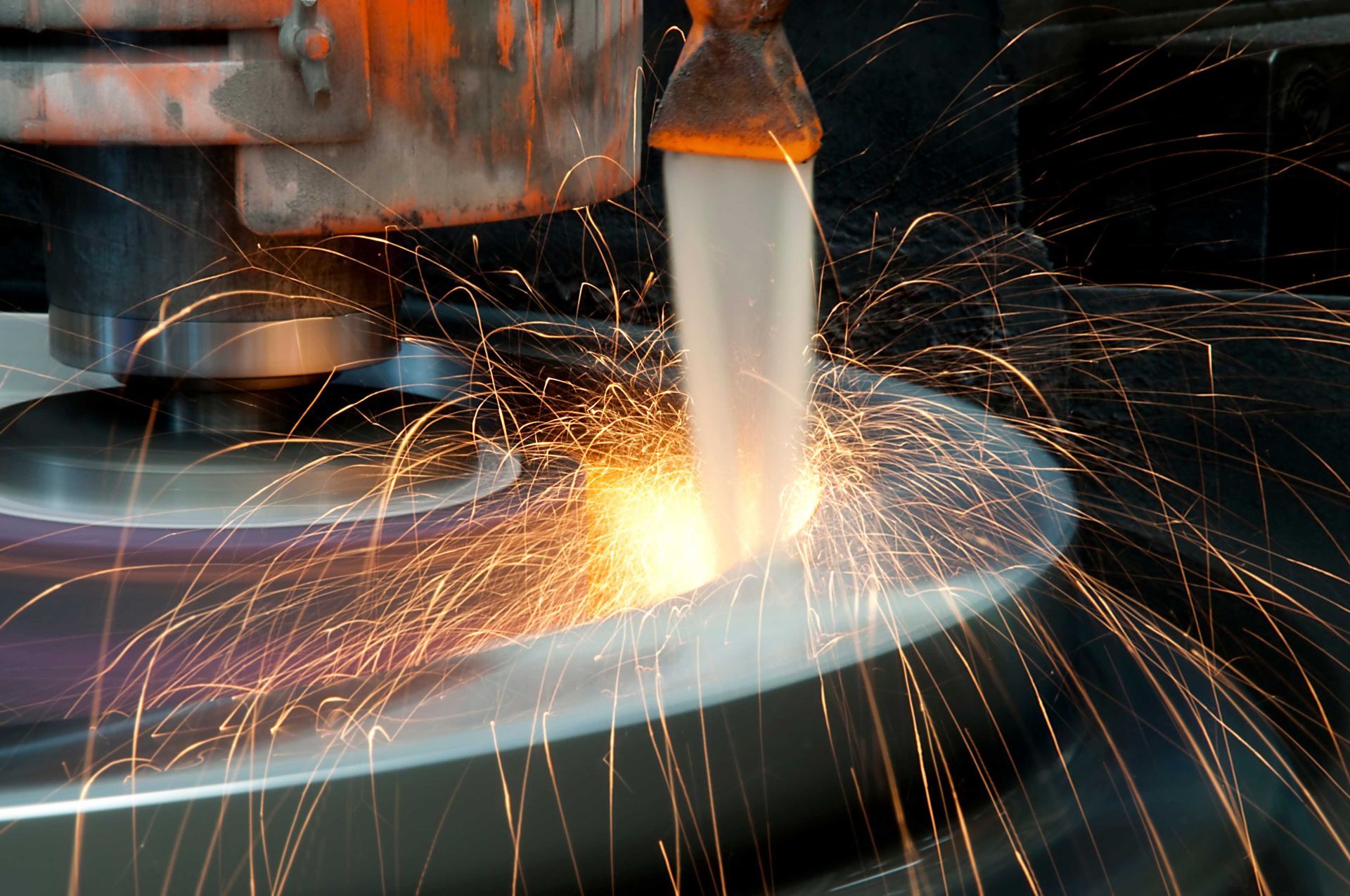 Sparks fly as a metal disc is ground by a machine, close-up view, workshop.
