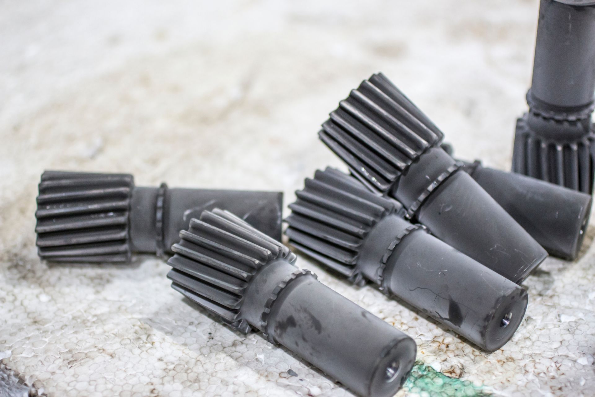 Close-up of several dark metal gears lying on a rough, light-colored surface.