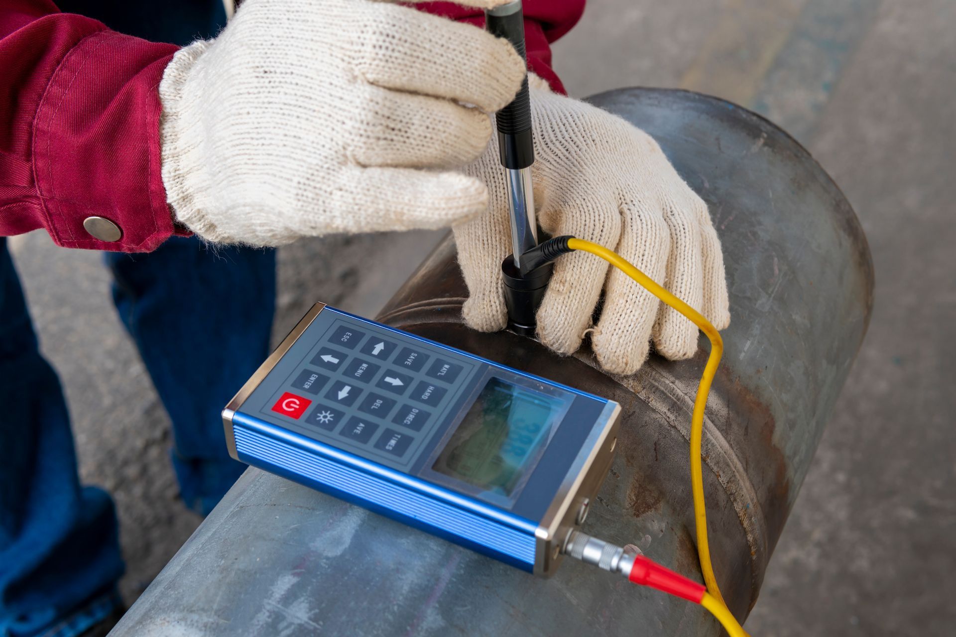 Person in gloves using an ultrasonic flaw detector on a metal pipe, testing for defects.