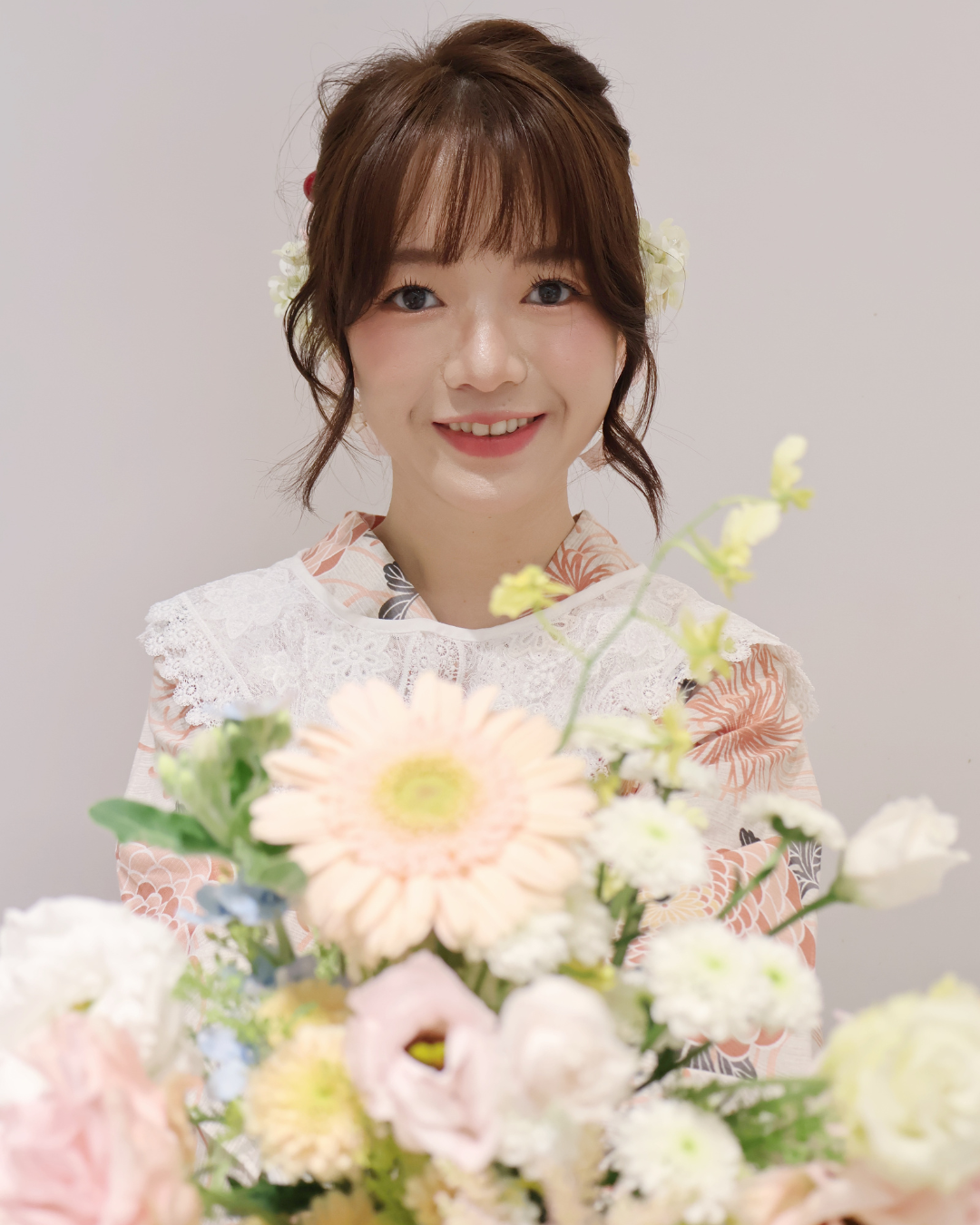 一束由白色、粉紅色和藍色花朵組成的柔和色調花束，襯托著一件淡粉色連身裙。