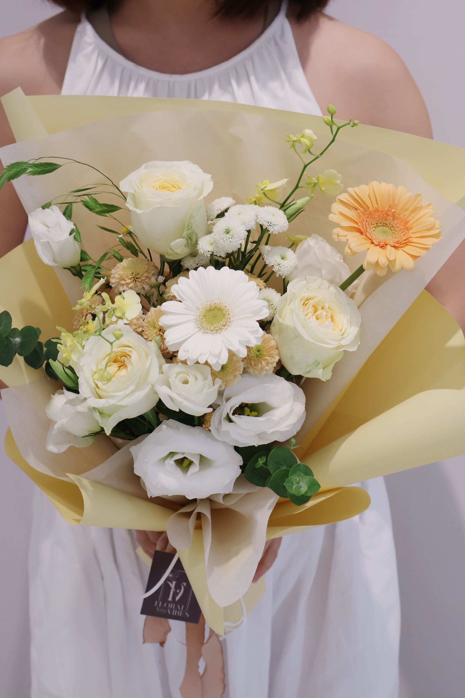 一位女子手捧一束用黃紙包裹的白色和黃色花朵。
