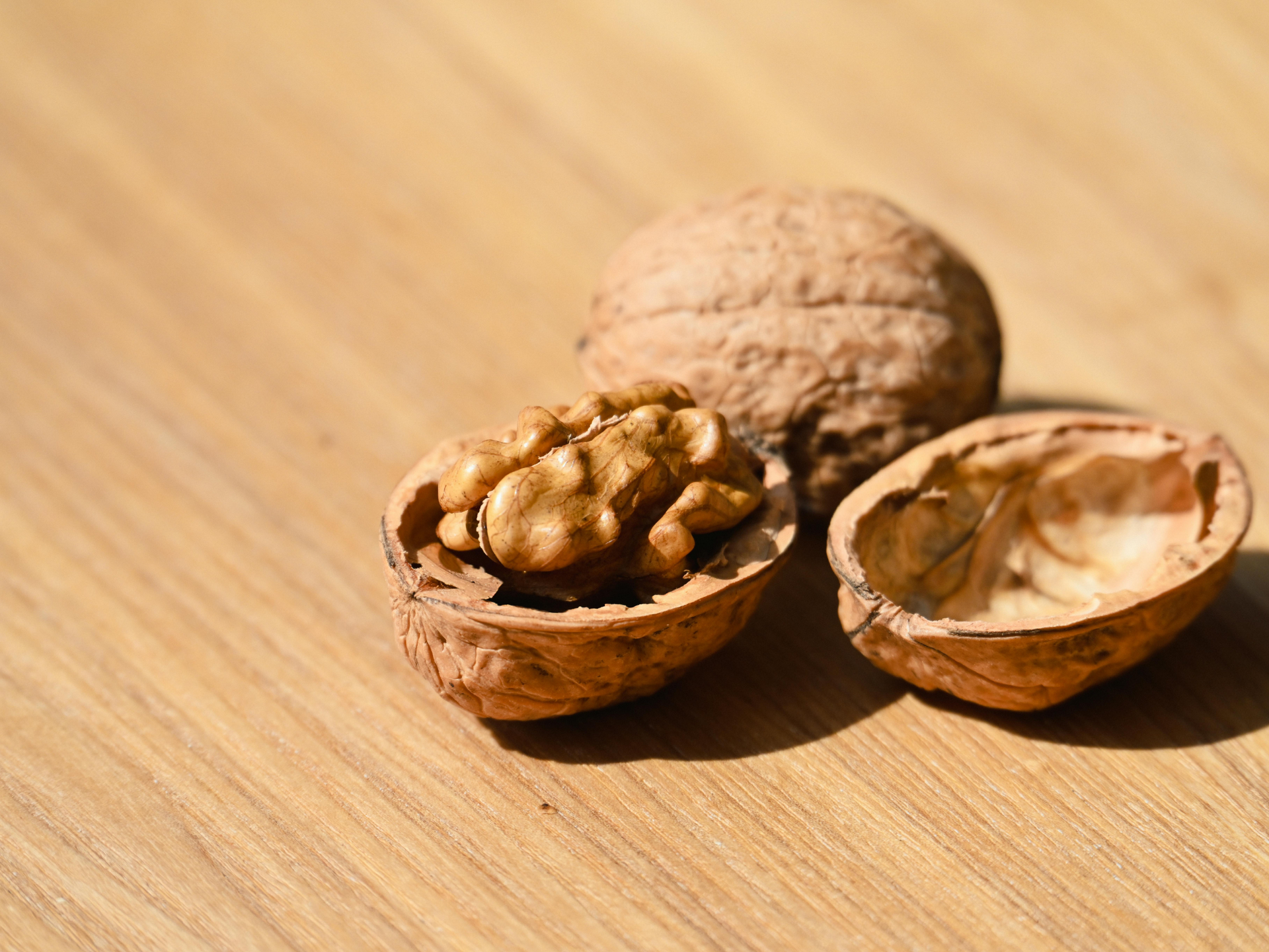 Walnuts in shells on a wooden table, with one whole walnut and two halves, one filled with kernels