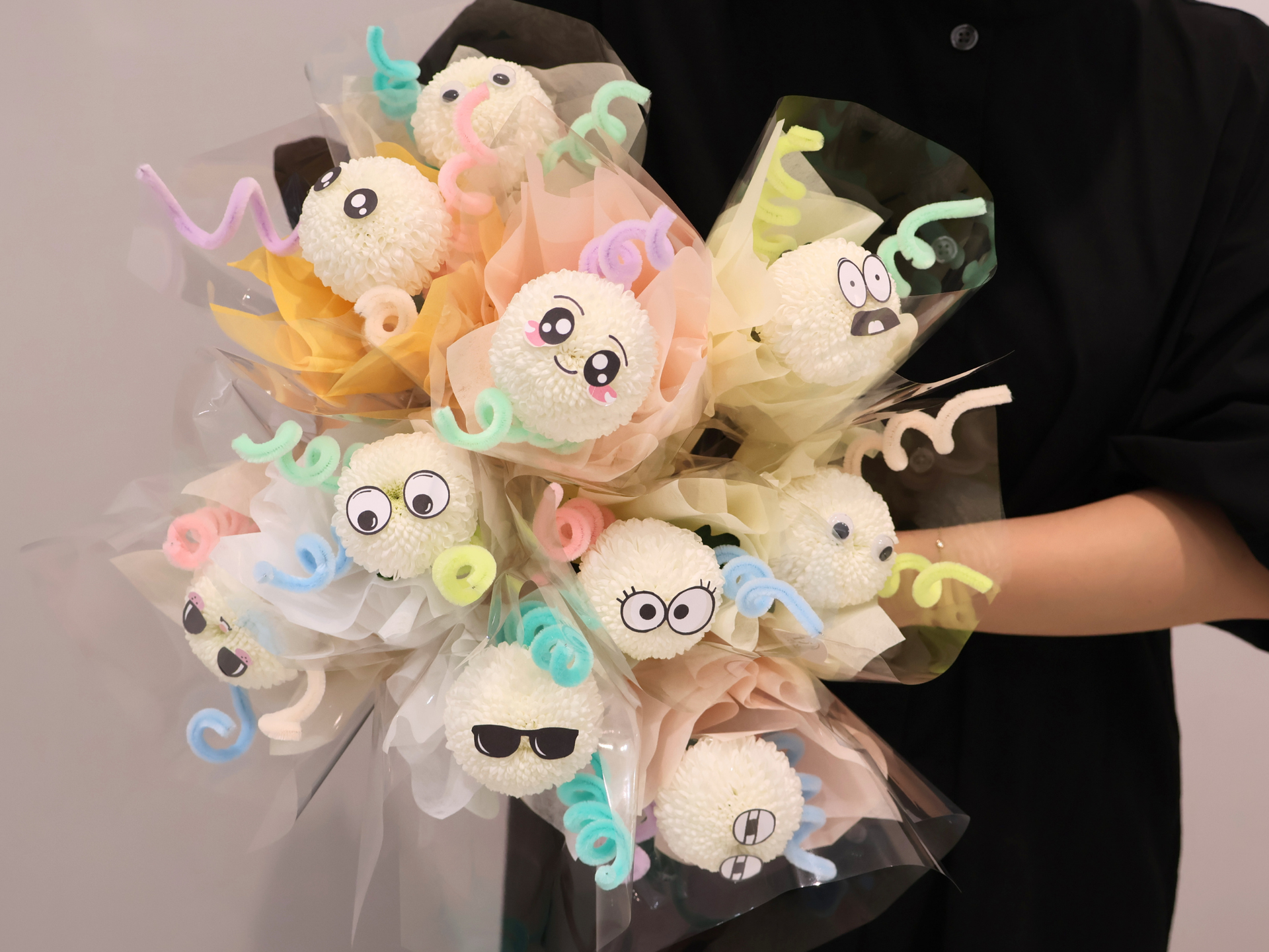 Pastel plush character bouquet wrapped in clear cellophane, held by a person in black.