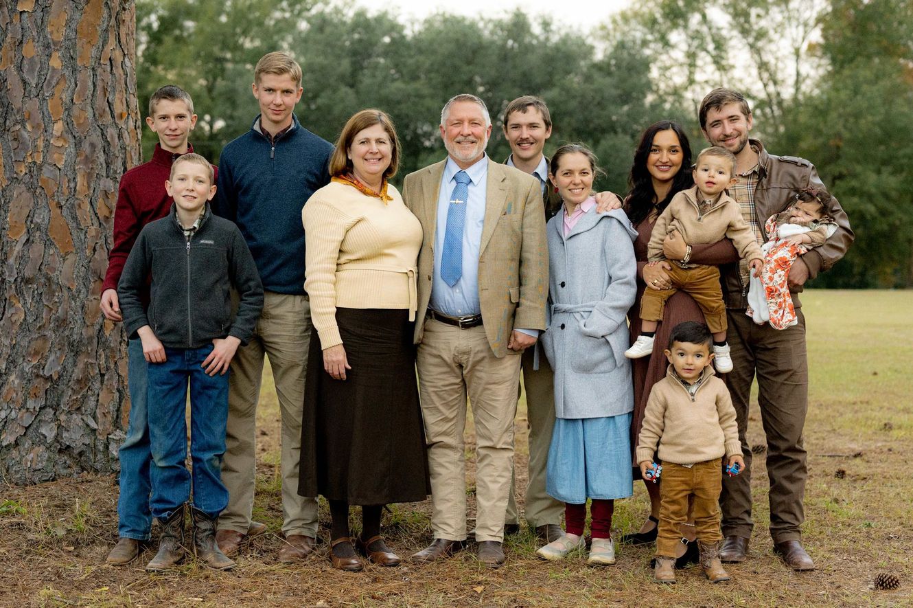 A family group posing outdoors on grass in autumn, dressed in formal and casual clothing.