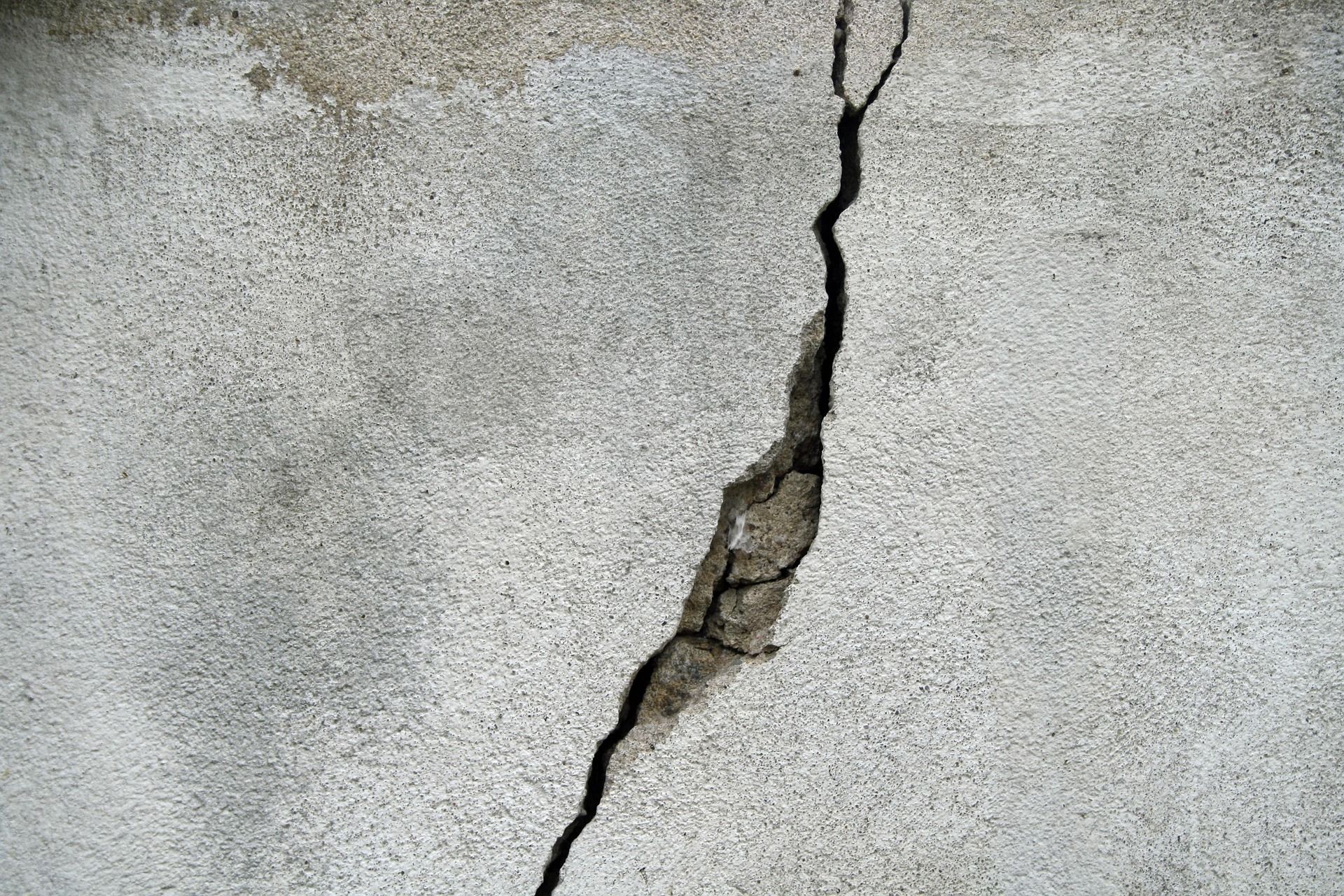 Cracked gray concrete wall with a large vertical fracture exposing rough inner material