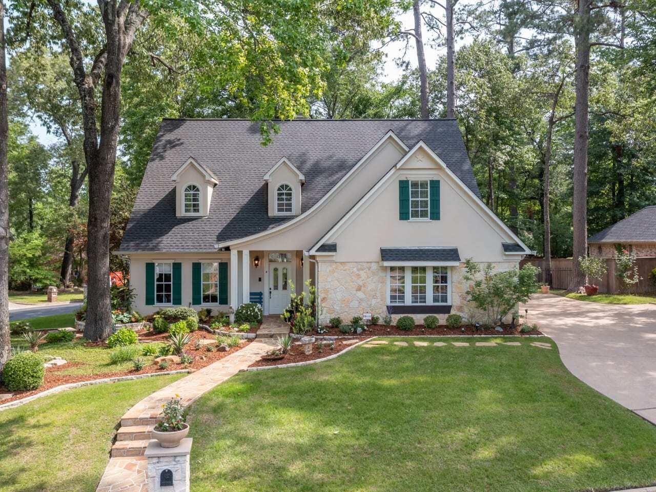 Suburban house with gray roof, white siding, green shutters, and a landscaped front yard in Longview TX