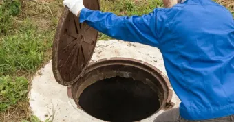 Worker in blue protective clothing lifting a manhole cover over an open sewer hatch