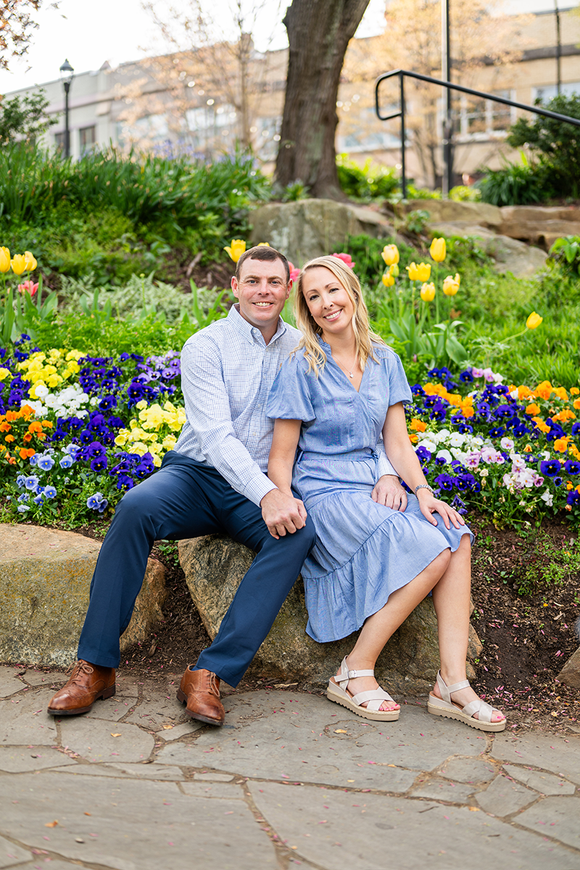 A man and a woman are sitting next to each other in front of a flower bed.