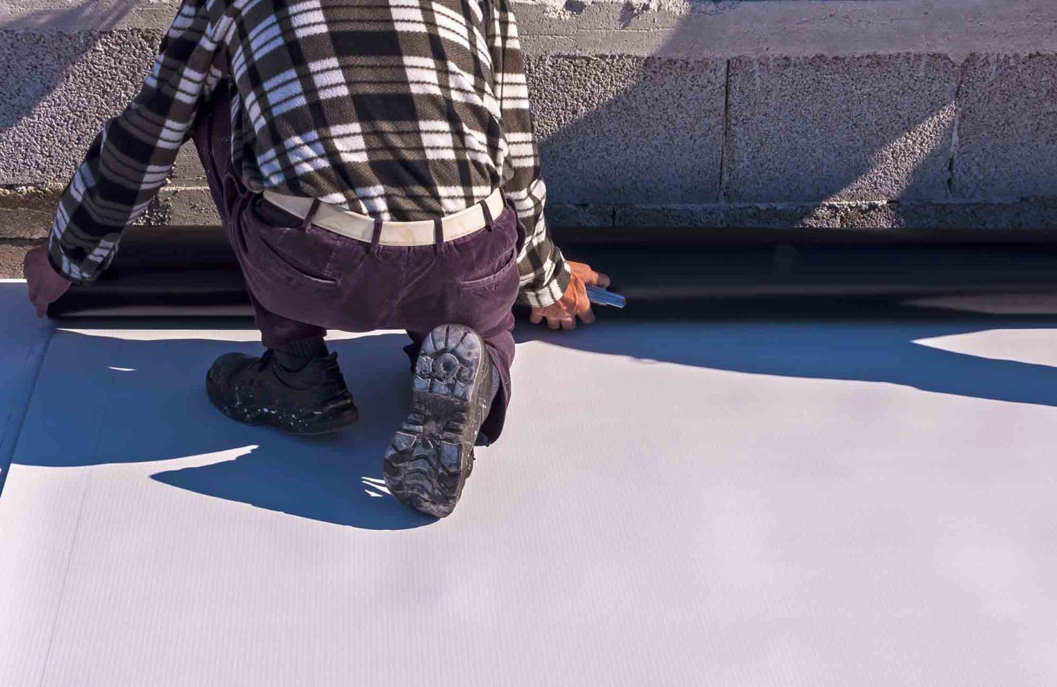 a man in a plaid shirt is kneeling down on a flat roof