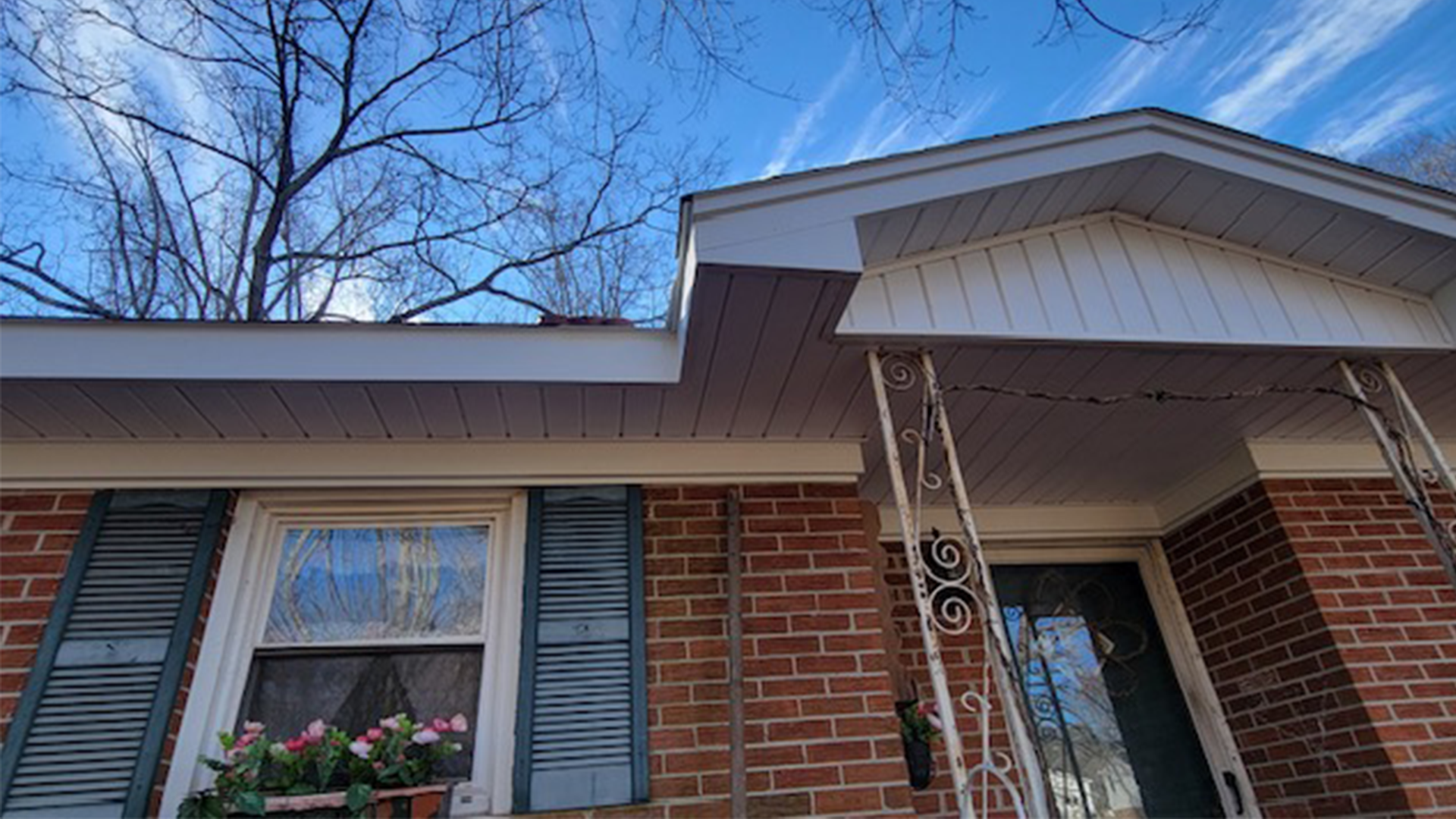 A brick house with a porch and a blue sky in the background.