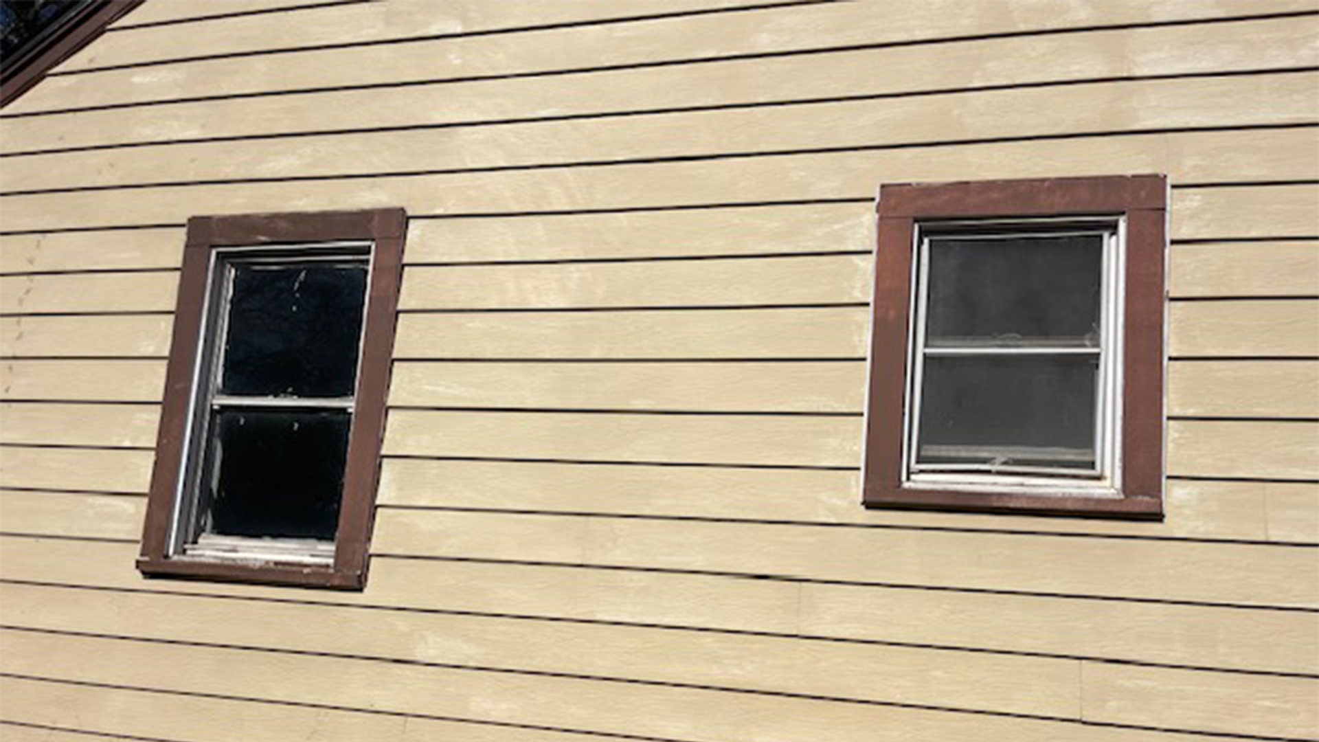 Two old windows on the side of a house with brown trim