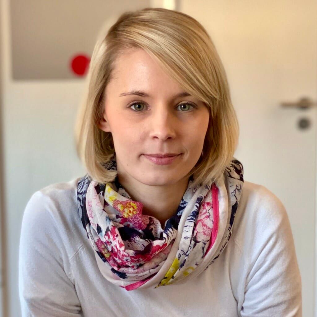 Eine Frau mit weißem Hemd und Schal blickt in die Kamera.