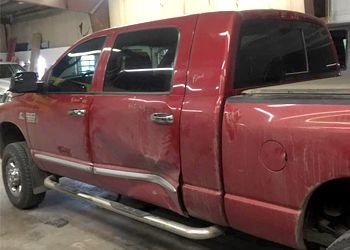 a red truck with a damaged side is parked in a garage .