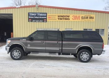 a gray truck with a black canopy is parked in front of a building .