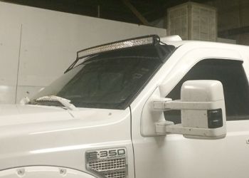 A white truck with a light bar on the hood is parked in a garage.