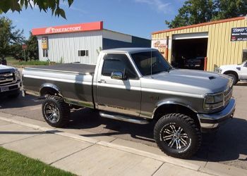 A silver truck is parked on the side of the road in front of a tire factory.