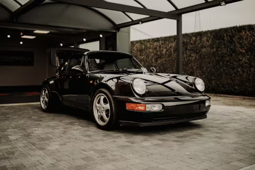Black classic Porsche 911 parked under a covered driveway, front three-quarter view.